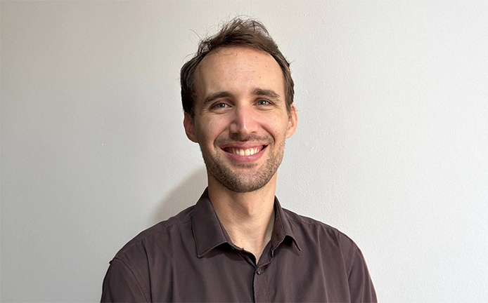 A man with a beard and brown shirt smiling.