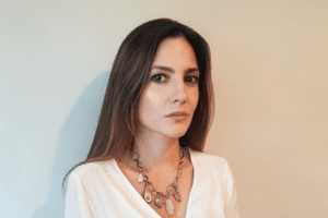 A woman wearing white shirt and necklace standing in front of wall.